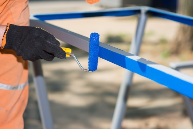 Werknemer in handschoenen met een roller schildert metaalblauw