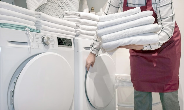 Werknemer in het hotel houdt veel handdoeken in handen in de buurt van Droge machine in de wasserij