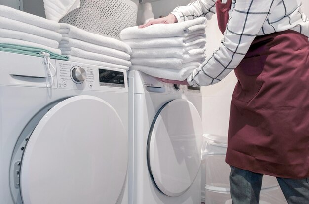 Werknemer in het hotel houdt veel handdoeken in handen in de buurt van droge machine in de wasserij