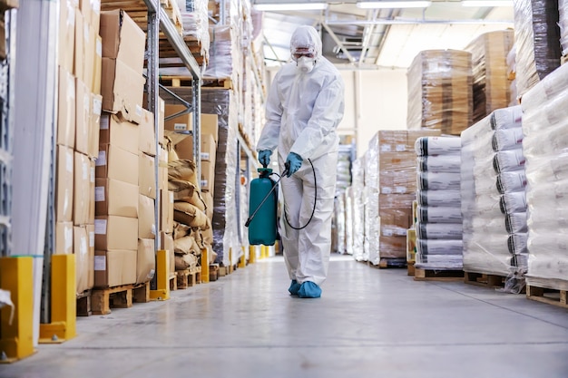 Werknemer in steriel uniform met rubberen handschoenen met sproeier met desinfectiemiddel