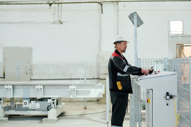 Werknemer in uniform die aan de machine staat en het productiewerk in de fabriek controleert