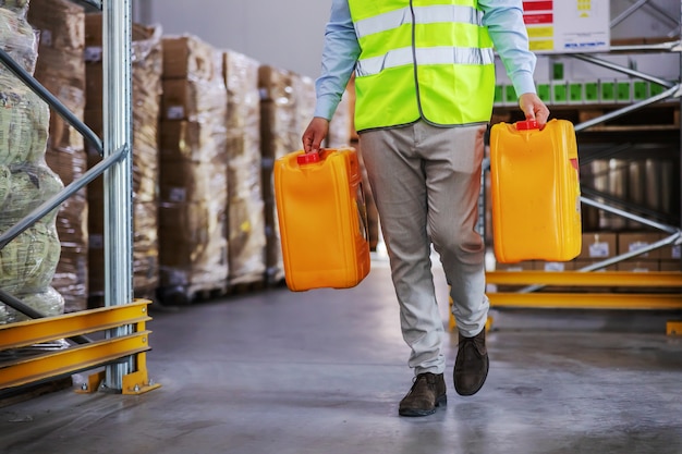 Werknemer in vest blikjes met olie verplaatsen tijdens het wandelen in magazijn.