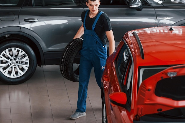 Werknemer in zwart en blauw uniform houdt autowiel vast en loopt in bijna rode auto