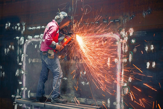 Werknemer met behulp van elektrisch wiel vonkslijpen op lasser metalen koolstofstalen deel schaalplaat in tank beperkte ruimte