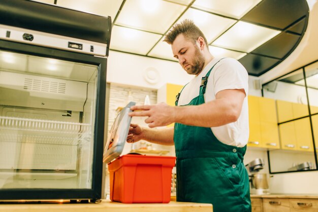 Werknemer met gereedschapskist reparatie koelkast thuis. Reparatie van koelkastbezetting, professionele service