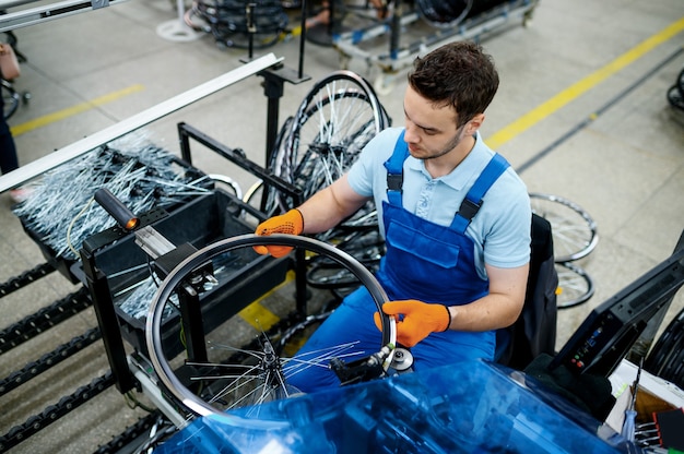 Werknemer met werktuigmachine installeert nieuwe fietsspaken op fabriek. Montage fietswielen in werkplaats