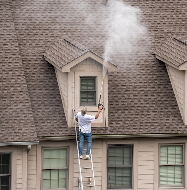 Werknemer op ladderdrukreiniging naar huis voorafgaand aan het schilderen