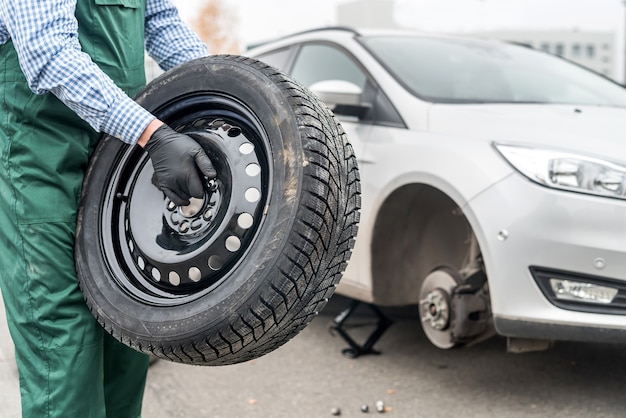 Werknemer reservewiel in de buurt van gebroken auto te houden