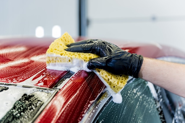 Werknemer rode auto met spons op een wasstraat wassen.