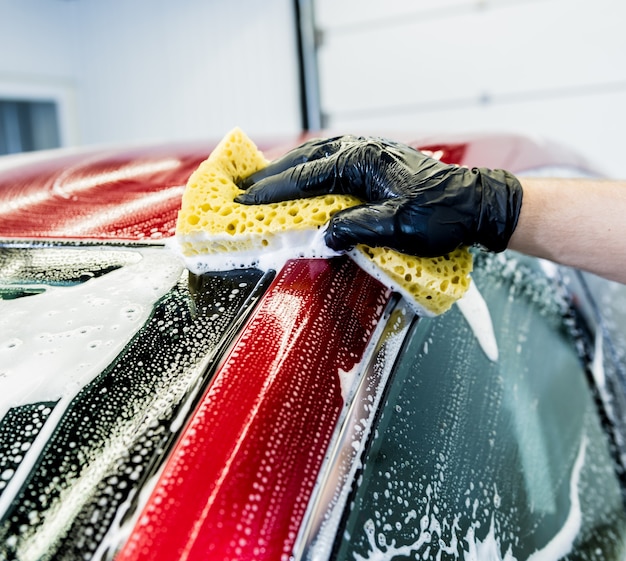 Werknemer rode auto met spons op een wasstraat wassen.