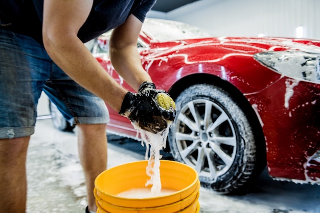 Werknemer rode auto met spons op een wasstraat wassen.