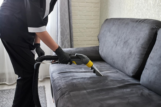 Werknemer schoonmaakservice bedrijf vuil verwijderen uit meubels in flat met professionele apparatuur Vrouwelijke huishoudster arm schoonmaken bank met wassen stofzuiger close-up