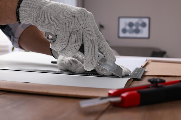 Werknemer snijden papier met mes en liniaal aan houten tafel binnenshuis close-up