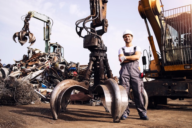 werknemer staat bij hydraulische industriële machine die wordt gebruikt voor het optillen van schrootdelen in schroothoop