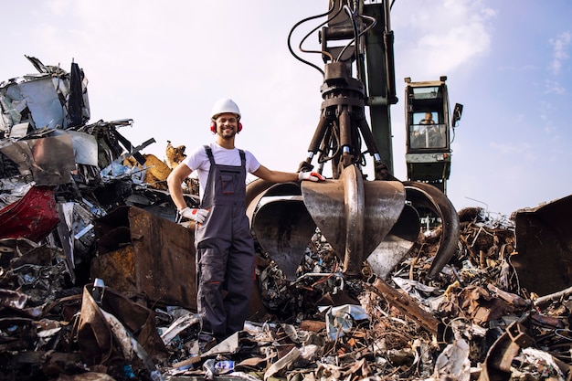 werknemer staat bij hydraulische industriële machine die wordt gebruikt voor het optillen van schrootdelen in schroothoop