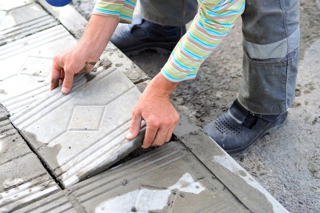 Werknemer tegelzetter legt tegels met cement buiten op zomerdag Authentieke workflow Handen met tegenoverliggende tegels