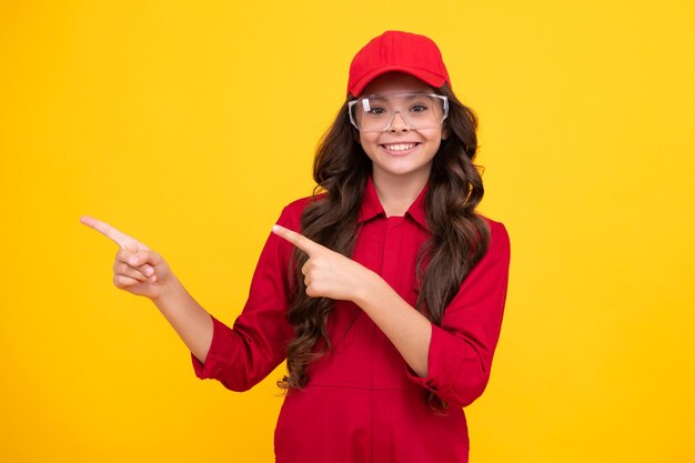 Werknemer tiener kind dragen overall rode dop en beschermen bril Studio shot portret geïsoleerd op gele achtergrond Wijzen en tonen concept