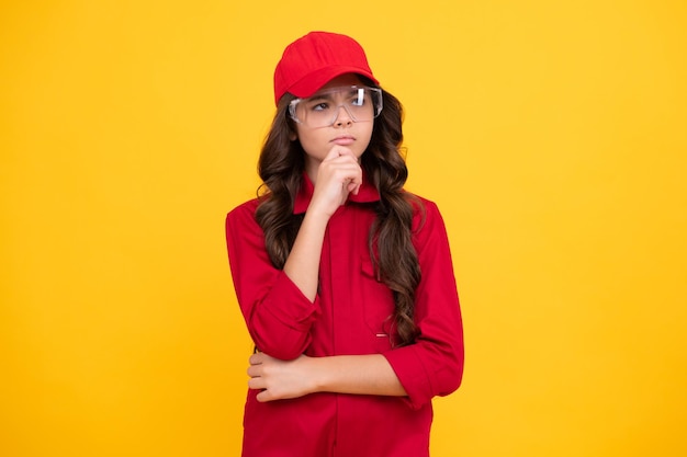 Werknemer tiener kind overall rode dop dragen en bril beschermen Studio shot portret geïsoleerd op gele achtergrond Denken peinzende slimme tiener meisje