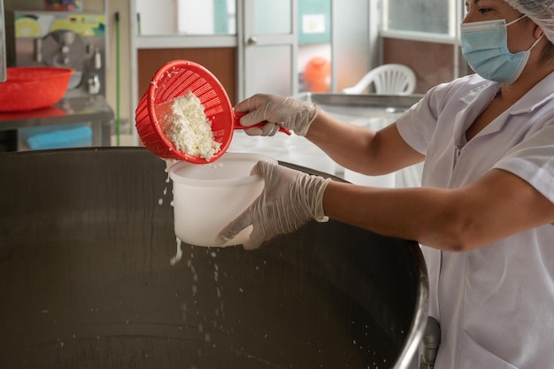 Werknemer verzamelt verse kaas uit een tank in een fabriek