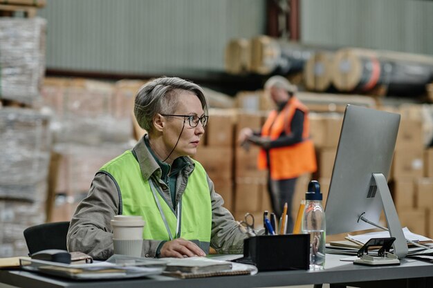 Werknemer zit op haar werkplaats in een magazijn en werkt aan een computer