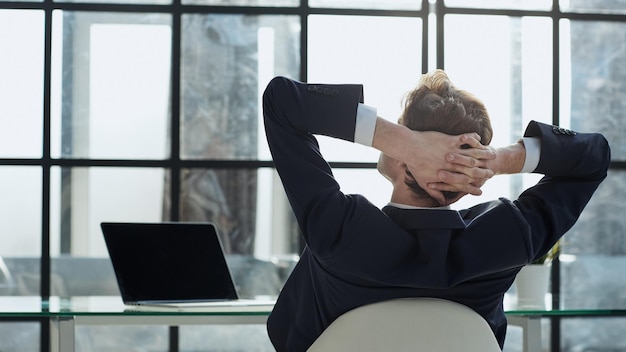 Foto werknemer zit op kantoor met de handen achter zijn hoofd