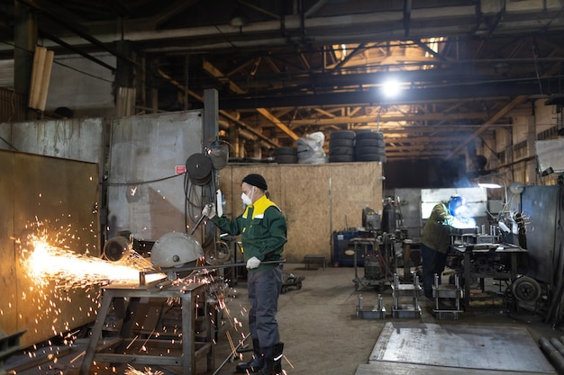 Werknemers die werken met metalen constructie op fabriek Metaalverwerking met grote haakse slijpschijfzaag en lasser lassen Vonken in metaalbewerking in fabriek