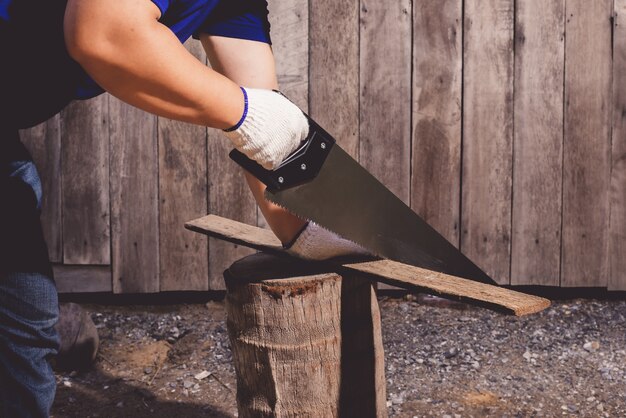 Werknemers in de bouw in blauw shirt met beschermende handschoenen werken met zaag