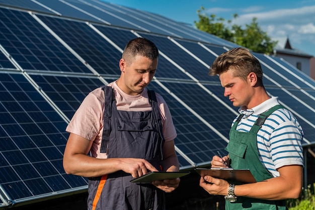 werknemers staan in de buurt van zonnepanelen en kijken naar een notebook