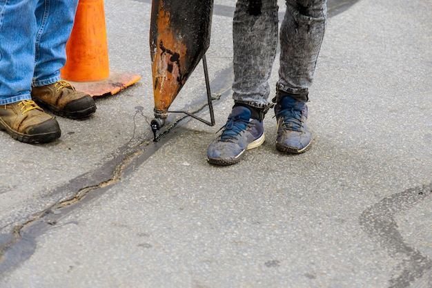 Werknemers voeren kleine reparaties aan bestrating uit door vloeibaar asfalt in putten op wegen die scheuren in de wegenbouw afdichten