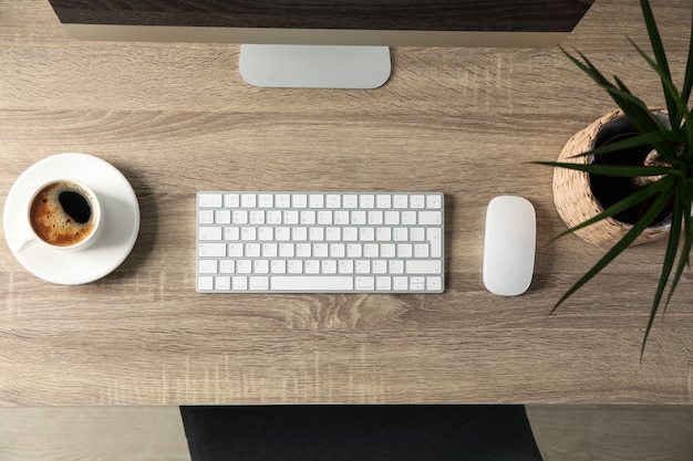 Werkplek met computer, kopje koffie en plant op houten tafel, bovenaanzicht