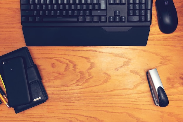 Foto werkplek. op een houten tafel bevinden zich: toetsenbord, computermuis, smartphone, kaarthouder, potloden en een nietmachine. hoge kwaliteit foto