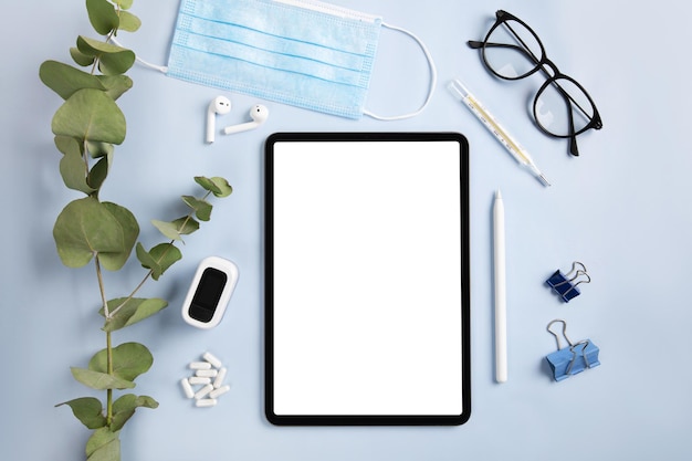 Werkplek tijdens quarantainetijd met tablet, masker, thermometer en oxitometer staan op tafel