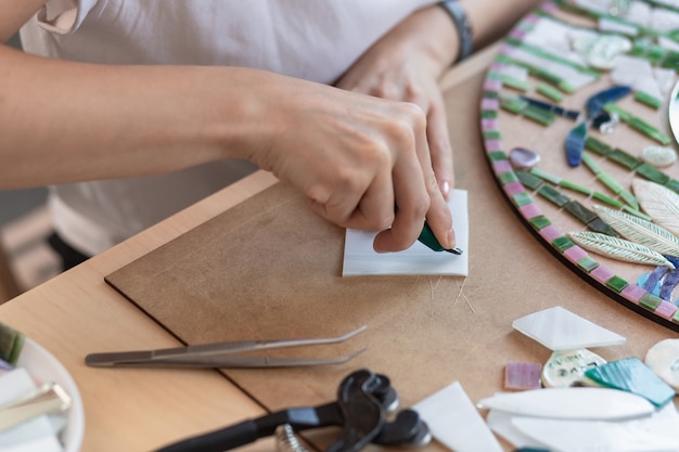 Werkplek van de handen van de mozaïekmeester die het gereedschap vasthoudt voor mozaïekdetails tijdens het maken van...