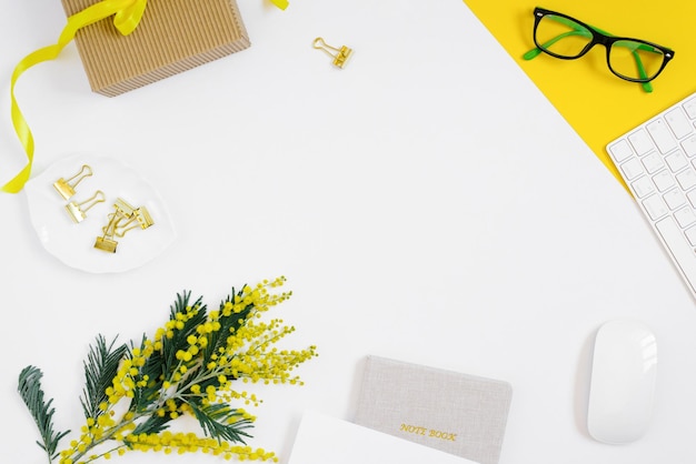 Werkplek van een vrouwelijke blogger is plat lag Briefpapier bril mimosa tak kladblok toetsenbord op witte achtergrond met kopieerruimte