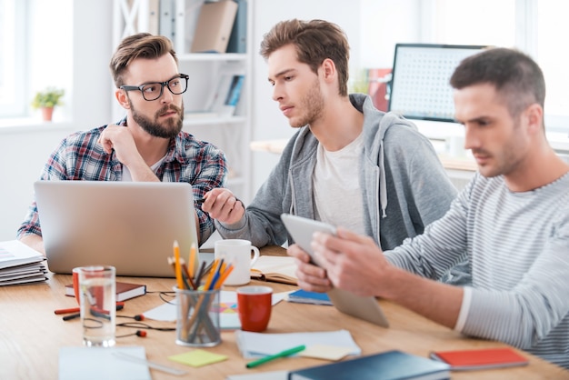 Werkproces. Drie jonge zakenmensen die samenwerken terwijl ze op hun werkplek op kantoor zitten