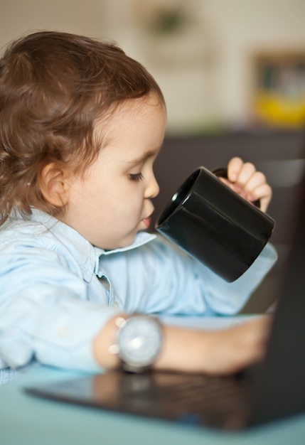 Werkruimte bureau met laptop. Weinig leuk bedrijfsmeisje dat bij lijst zit en een mok koffie drinkt. Kid online leren. Afstandsonderwijs online onderwijs.