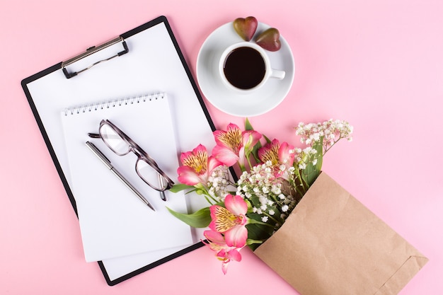 Werkruimte met kopje espresso, notebook, tablet, glazen en bloemen van gipskruid en Peruaanse lelie op een roze achtergrond