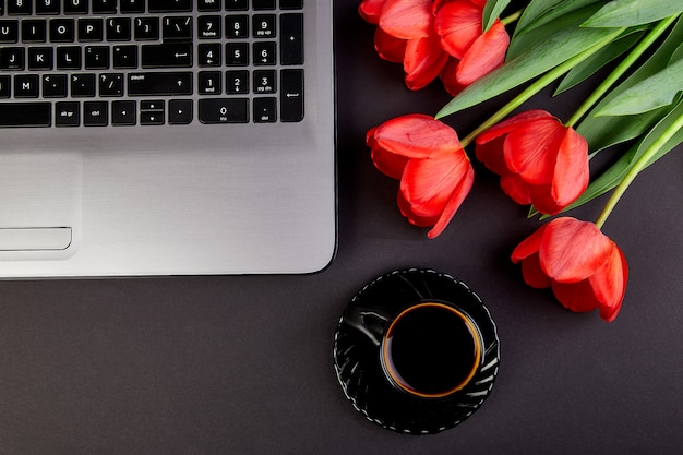 Werkruimte met laptop, rode tulpen en zwarte koffie