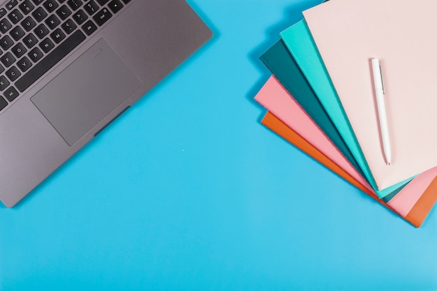 Werkruimte met laptop toetsenbord en kleurrijke notebooks op blauwe tafel. bovenaanzicht