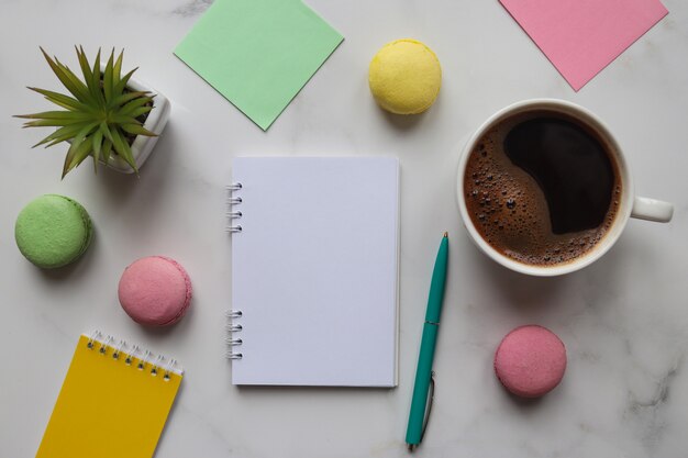 Werkruimte met notitieboekjes, potloden, pen, plant, kopje koffie en bitterkoekjes op marmer