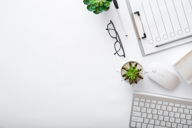 Werkruimte met toetsenbord muis bril papieren groene planten. Plat lag Wit bureau thuiskantoor werkplek pc computer. Witte tafel kantoor bovenaanzicht met kopie ruimte.