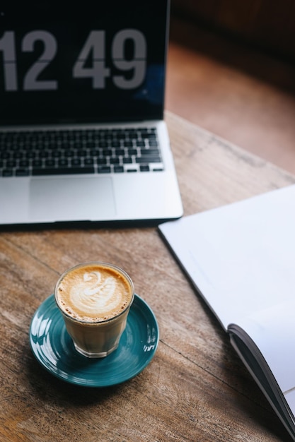 Werkruimte met warme koffiekop, laptop en lege notitie op houten tafel.