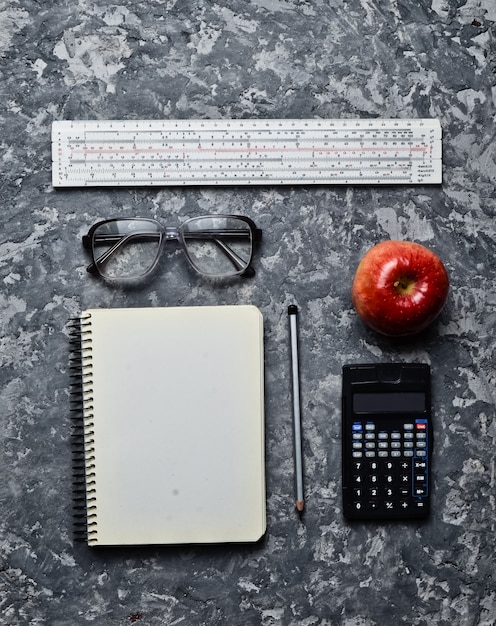 Werkruimte van een student ingenieur op een betonnen ondergrond. Loft-stijl. Kladblok, appel, rekenmachine, potlood, bril, liniaal. Minimalisme en trend van grijze kleur. Bovenaanzicht Plat leggen.