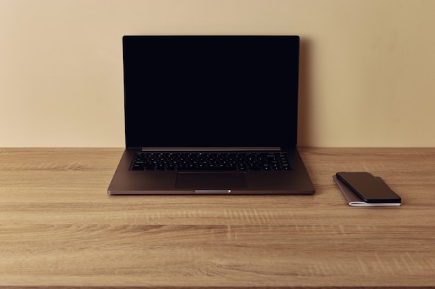Werkruimtebureau, laptop met leeg scherm en mobiele telefoon. Kopieer ruimte op beige muur.