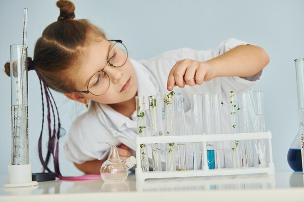 Werkt met vloeistof in reageerbuizen Klein meisje in jas speelt een wetenschapper in het laboratorium met behulp van apparatuur