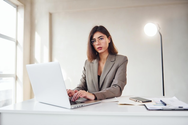 Werkt op kantoor met laptop Jonge vrouw in formele kleding is binnenshuis Conceptie van stijl