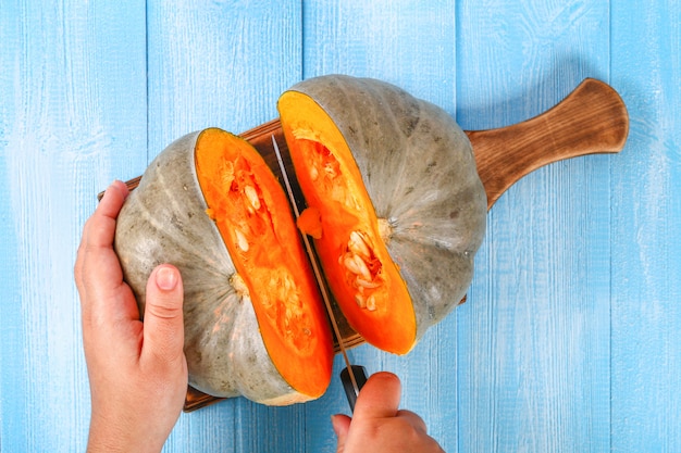 Werkwijze voor het snijden van pompoenstukken voor het koken van pompoensoep of puree. pompoen op een blauwe houten tafel