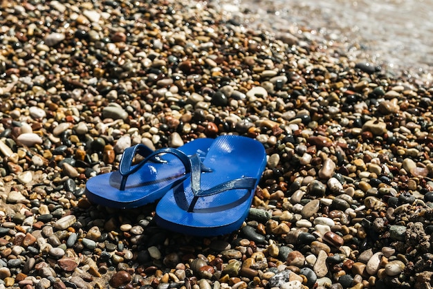 小石のビーチで濡れた青いゴム製フリップフロップ