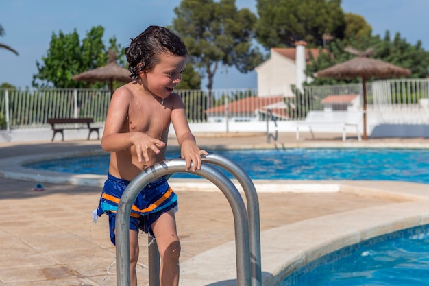 Wet boy just out of the pool looks into the water and smiles with amusement