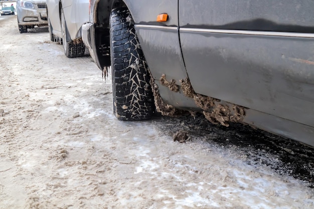 車にくっついた濡れた汚れた雪 泥で覆われた塩辛い灰色の車のクローズアップ